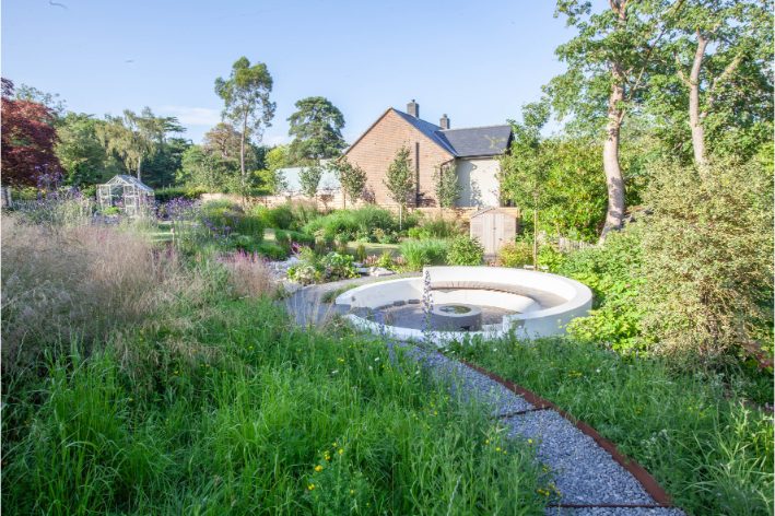 View across airy planting and large descending gravel steps to round sunken seating area. 