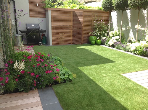 Small garden with lawn, wooden decking, porcelain tile edging and planted beds. Design by Harrington Porter.