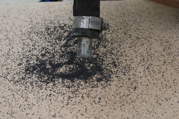 Sawn natural stone being given a surface finish of sandblasting. Black sand directed by metal nozzle. 